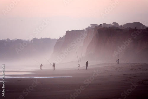 Misty sunset beach with fisherman silhouettes Algarve Portugal