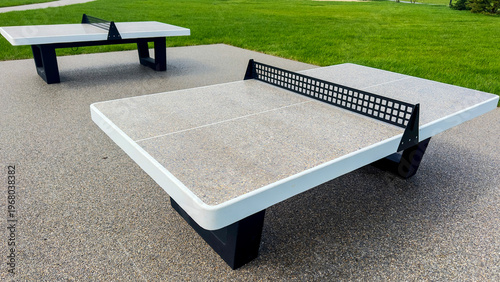 Outdoor ping pong tables sit on gravel near grass
