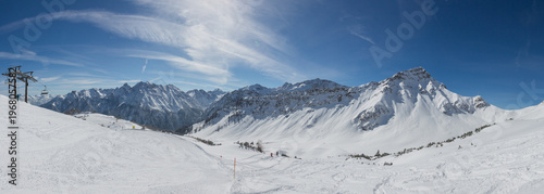 Chairlift at European Alps at skiing area Brandnertal, snowy mountains with blue sky (panorama)