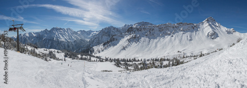 Chairlift at European Alps at skiing area Brandnertal, snowy mountains with blue sky (panorama)