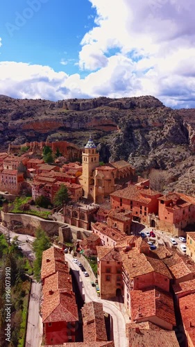 Panoramic elevated view of Albarracin medieval village in Aragon, Spain, showcasing red-stone buildings, cathedral tower, and dramatic rocky cliffs