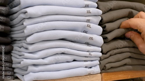 Hand chooses clothes on shelves in the store close-up.