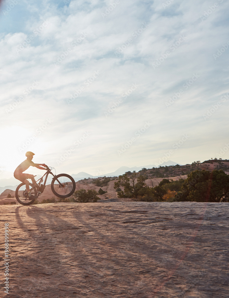 Fototapeta premium Man, mountain bike and fitness with speed for wheelie for extreme sport, cycling or space in nature. Person, bicycle and cardio training in sunshine for stunt, safety gear and exercise in countryside