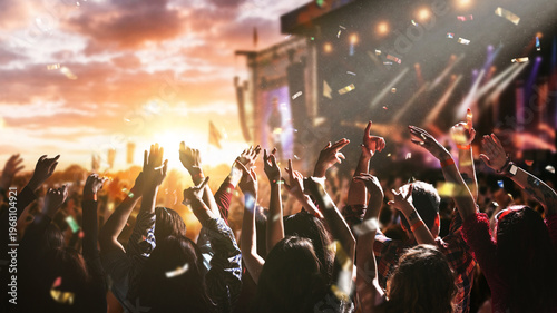 Fotografie Large crowd dancing and celebrating at music festival stage with confetti and sunset sky