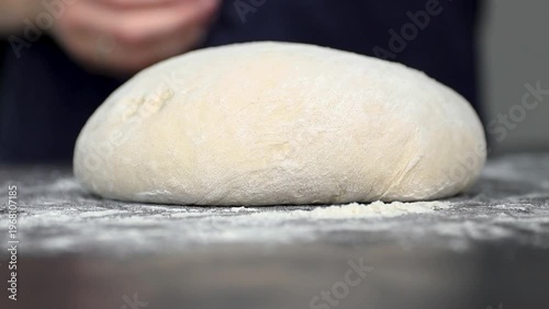 Hands of a person gently kneading dough on a floured surface, with a striped cloth partially covering the dough in a bright kitchen setting