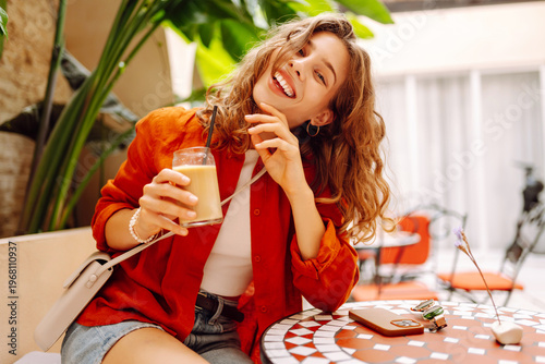 Foto A portrait of a young woman sitting at a table in a sunny cafe, sipping a chilled drink on a sunny day