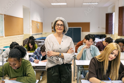 Konstfotografi Senior teacher smiling, standing with arms crossed, observing multicultural high