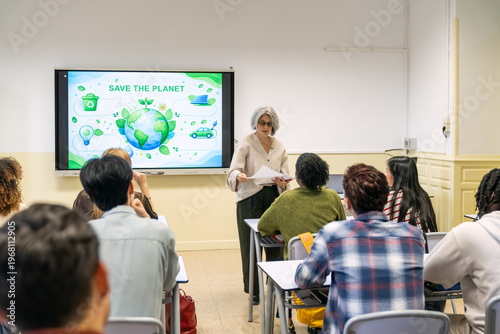 Teacher giving papers to diverse students in a classroom. Interactive whiteboard displaying a save the planet ecology presentation