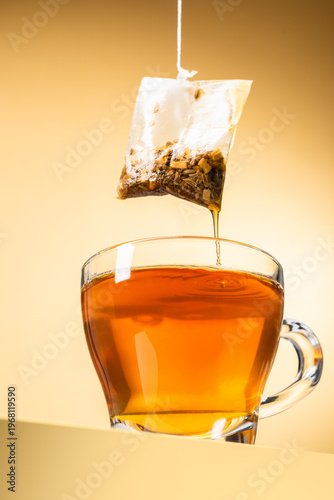 Glass cup of tea with dripping tea bag on yellow background