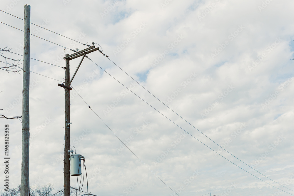 Fototapeta premium Electricity poles stand in the field under a cloudy sky with power lines connecting them to the grid in a rural area during the day