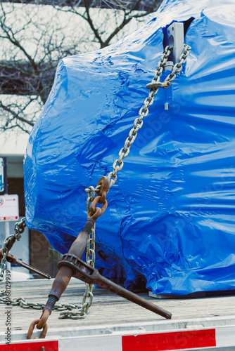 Foto Heavy equipment wrapped in blue plastic secured with chains on a flatbed truck i