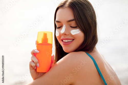 Woman Holding Sunscreen Bottle And Smiling At Beach With Sun Cream On Face. Skin Care And Sun Protection Concept