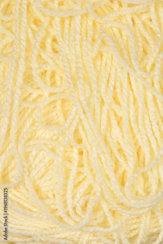 A detailed close up view shows the soft and twisted fibers of a messy pile of light yellow wool knitting yarn