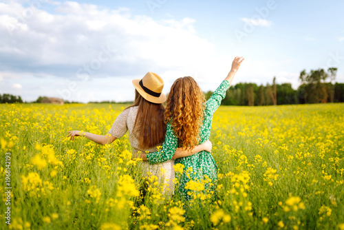 Cuadro en lienzo Two cheerful friends in dresses are having fun in a blooming field, bathed in sunlight