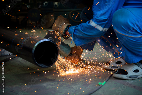 Worker cutting steel pipe with abrasive saw without proper safety footwear, highlighting unsafe working conditions, flying sparks, and potential workplace hazards in industrial environment.