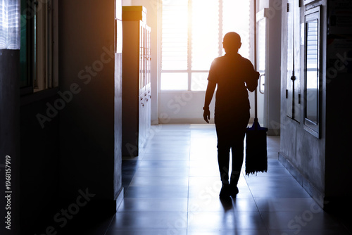 Janitor woman holding mop in hallway office building or walkway after school or classroom for clean floor. Silhouette housekeeper working job with sun light background.