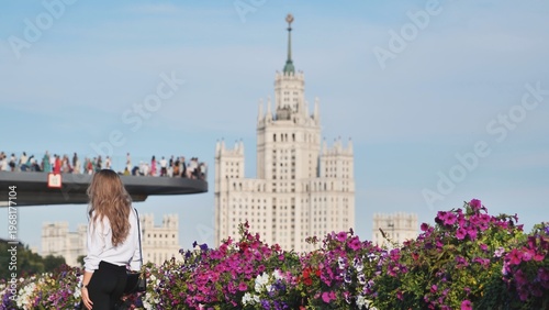 Photography Woman looking at the Stalinist skyscraper from a green city park with vibrant fl
