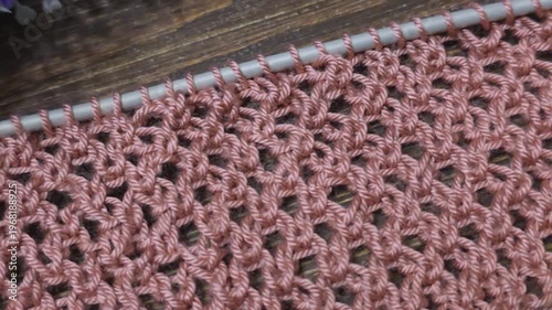 A textured, openwork knitting pattern made with colored yarn on a wooden surface with decorative flowers. Close-up of the knitting texture and pattern. Conceptual ideas for handicrafts