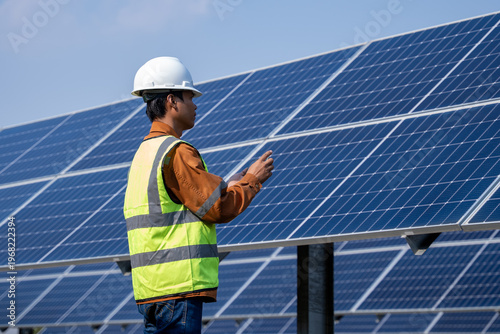 Technician inspect photovoltaic panels in a solar farm, wearing safety gear and monitoring system performance under clear sky conditions, ideal for renewable energy operations and maintenance visuals.