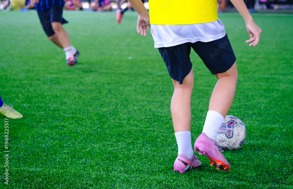 Fototapeta premium Young soccer player dribbling the ball during a friendly match on indoor field, action moment with blurred background, concept of youth football competition and teamwork.