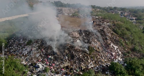 Aerial zoom in view. Burning rubbish causing greenhouse gas, contributor to climate change.  Extreme Poverty. People living alongside dumpsite struggling to survive through waste picking.
