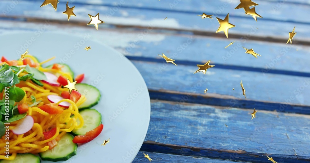 Fototapeta premium Displaying white ceramic plate with spiral noodles salad on worn blue table, gold stars, copy space