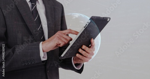 Holding tablet, businessman tapping screen at studio, wearing suit and tie with hologram globe