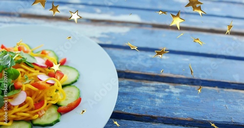 Displaying white ceramic plate with spiral noodles salad on worn blue table, gold stars, copy space