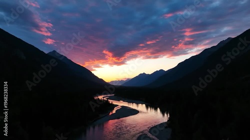 A breathtaking sunset paints the sky with vibrant colors over a winding river nestled between majestic, dark mountain ranges