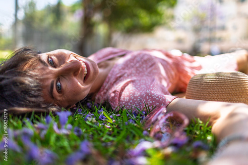 Summer mood. Young woman lies on green grass and flowers. Summer mood. Girl spends time outdoors. Girl smiles at camera.