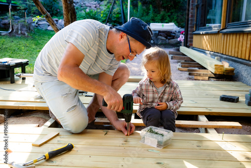Cuadro en lienzo Joyful father and little child building a wooden patio deck together
