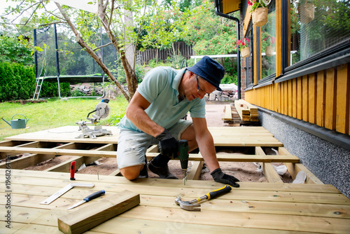 Foto Homeowner using a power drill to install wooden deck planks during a backyard renovation, capturing realistic DIY, woodworking, outdoor construction