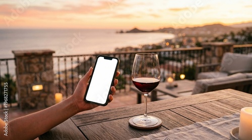 Hand holding smartphone with white screen beside glass of red wine on terrace. Concept of travel, luxury lifestyle, vacation booking, leisure, tourism and mobile communication. Generative AI.