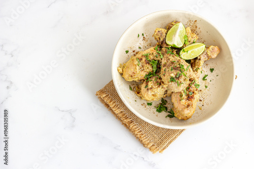 Creamy Spiced Chicken Drumsticks with Lime and Herbs in Bowl on Marble Background with Copy Space 