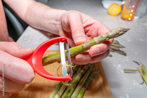 Tableau sur toile Peeling asparagus with a vegetable peeler over a cutting board in a kitchen environment