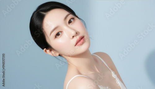 淡いブルー背景の前で首をかしげながら見つめる若い女性の透明感あふれるナチュラルビューティーポートレート