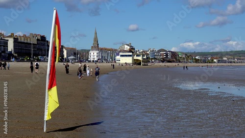 Weymouth,Dorset, UK, 31st March 2026 - Lifeguard flags blowing on Weymouth beach with town in B/G