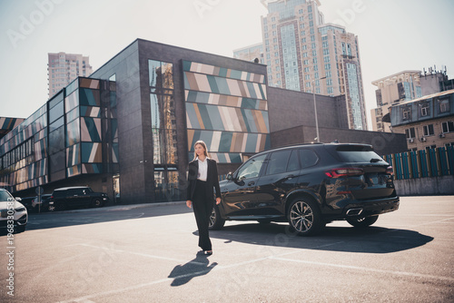 Photos Businesswoman walking past luxury SUV in modern urban parking lot by contemporar