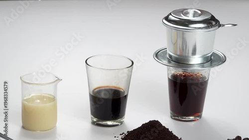 Wide shot of Vietnamese coffee ingredients including condensed milk, black coffee, and an active phin filter on a white background. Premium recipe footage.