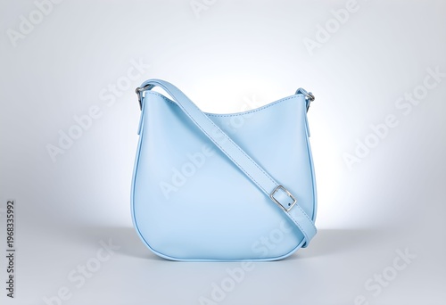 A stylish light blue leather bag with a strap is placed on a white surface.