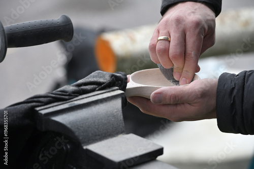Hands carving spoon from wood, working with sand paper close up.