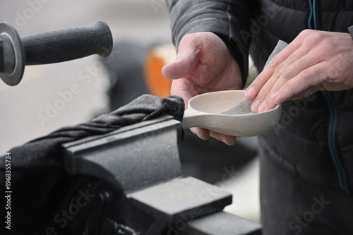 Hands carving spoon from wood, working with sand paper close up.