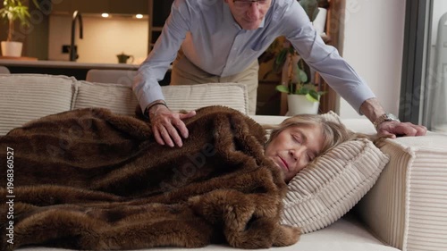 Senior man caring for sleeping woman on couch