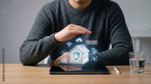 Man gestures toward holographic home security display. His hand hovers above a glowing digital shield. Table holds tablet, glass, and stylus