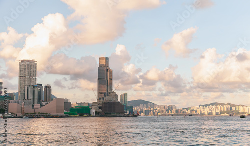 Warm sunset light bathes Hong Kong Harbour skyline, highlighting modern high‑rises, calm water and soft clouds. A peaceful urban seascape