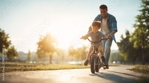Father teaching his son to ride a bicycle at sunset in park. Family bonding, childhood learning and happy lifestyle concept.