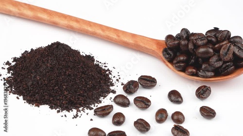 Tight rotating macro of whole roasted coffee beans on a wooden spoon next to ground coffee powder on white background. Premium ingredient concept for cafe menus and beverage projects.