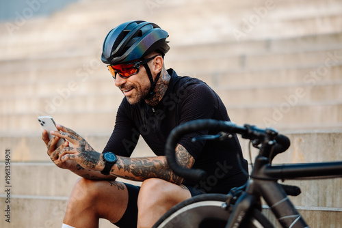 Male Cyclist Smiles While Looking At Device. Male Cyclist With Tattoos Happily Reading On Urban Ride