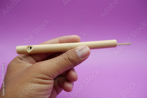 Hand Holding a Simple Wooden Whistle on a Soft Purple Background
