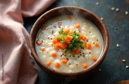 Hot Korean vegetable porridge in rustic bowl with chopped carrots and green onions. Rice and barley soup with fresh ingredients. Healthy meal for lunch or dinner.